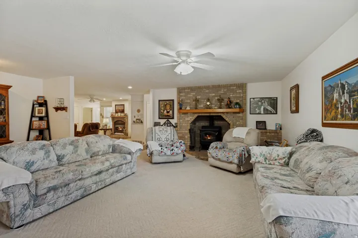 Spacious living room featuring multiple seating areas, neutral carpet flooring, and a brick fireplace with dark mantel