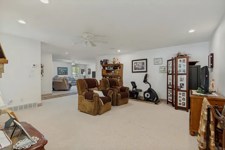 Spacious recreation room with neutral carpet flooring, ceiling fan with recessed lighting, and abundant natural light