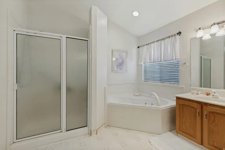 Corner soaking tub, separate shower with frosted glass enclosure, wood-finish vanity with countertop, and recessed lighting