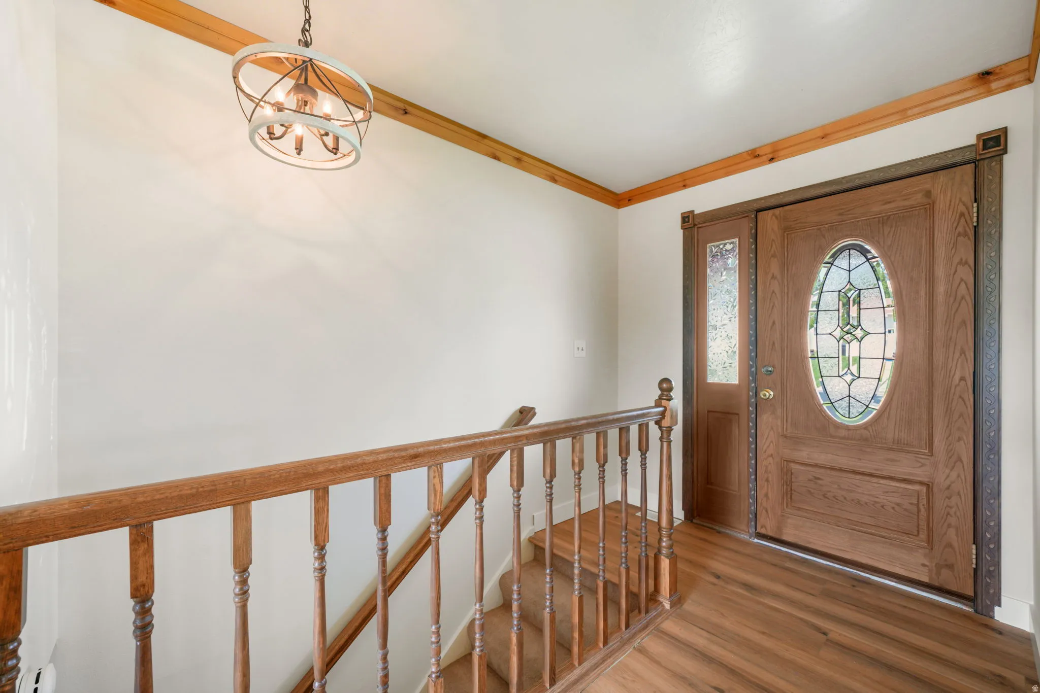 Welcoming foyer showcasing warm wood-finish flooring, decorative wrought iron stair railings with turned balusters, wood trim ceiling details, and a solid wood entry door with leaded glass oval window