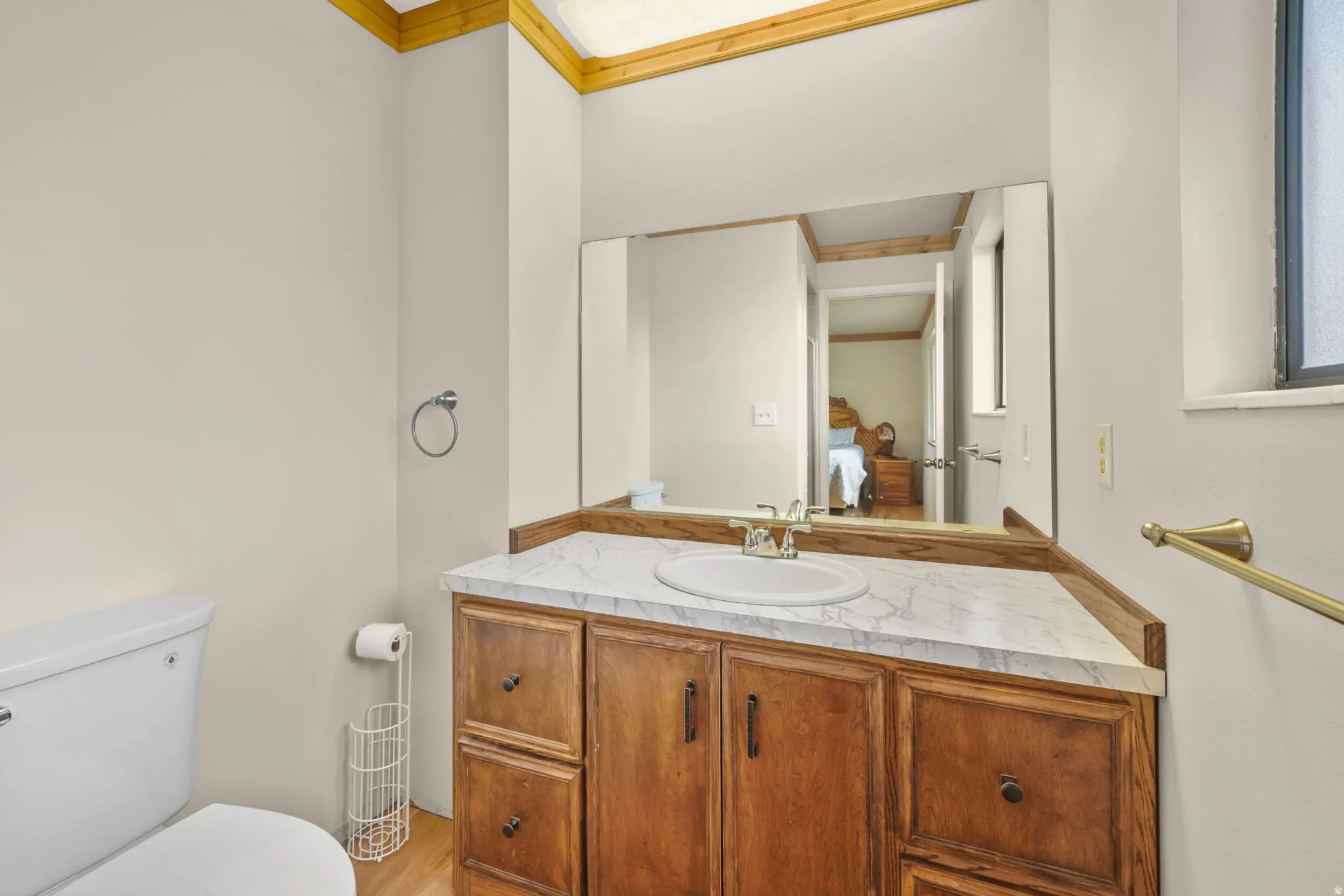 Master Bathroom - Elegant bathroom vanity featuring warm wood cabinetry with multiple drawers and cabinet storage, a white marble-finish countertop, and a large framed mirror with integrated lighting