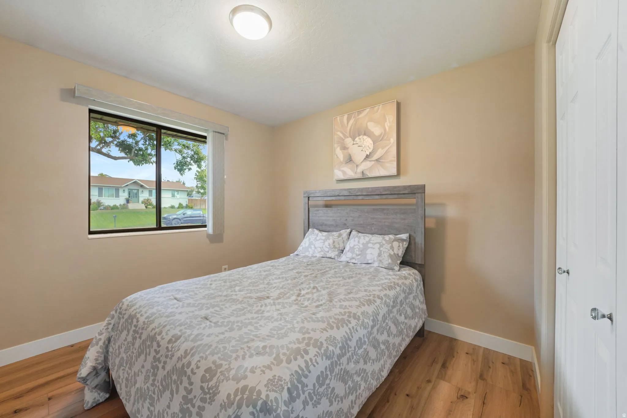 2nd Bedroom - Window with exterior neighborhood visibility, wood-finish flooring, neutral wall paint, ceiling-mounted light fixture, and white bi-fold closet doors