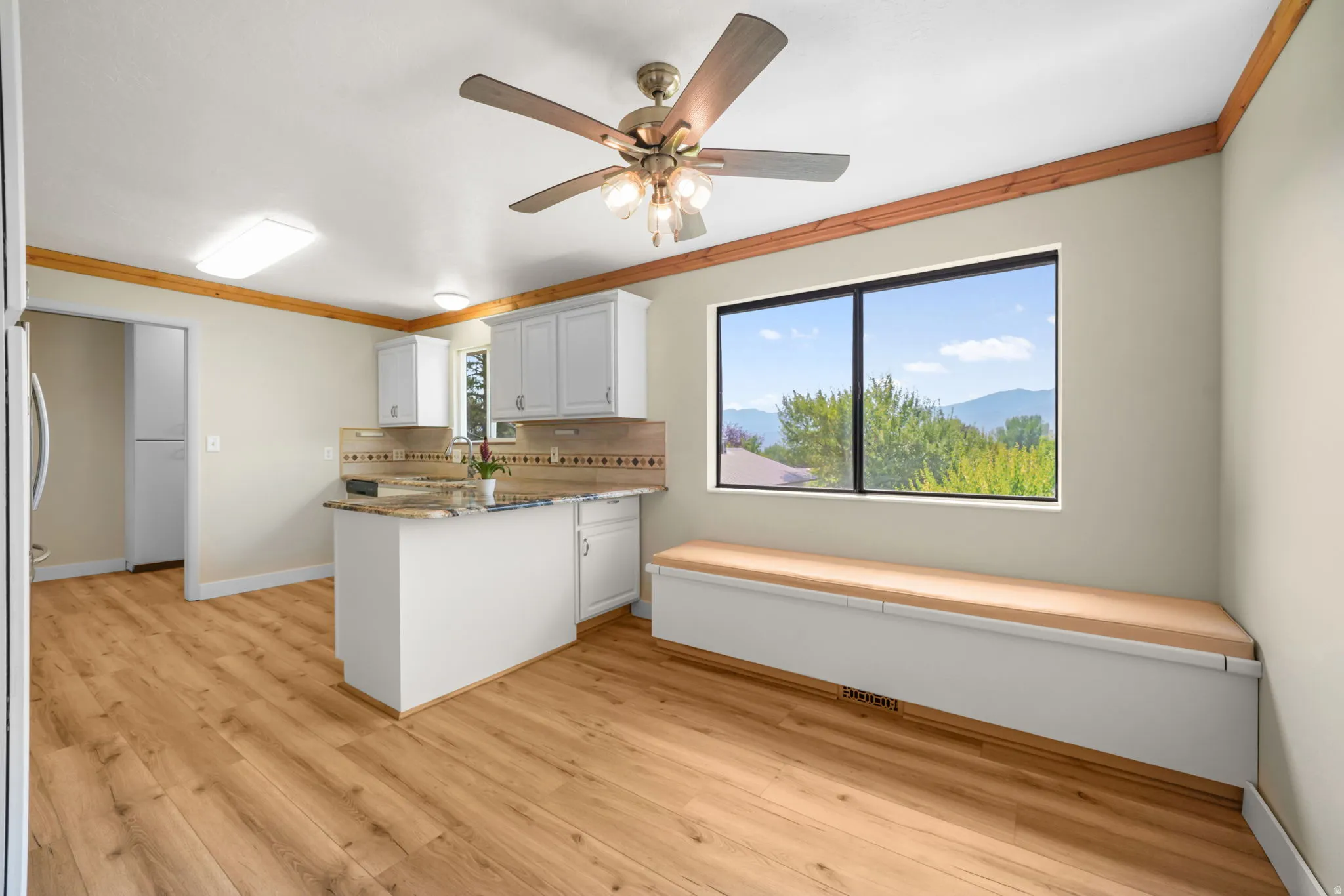 Wood-finish flooring throughout, white cabinetry, built-in window bench, and an overhead ceiling fan