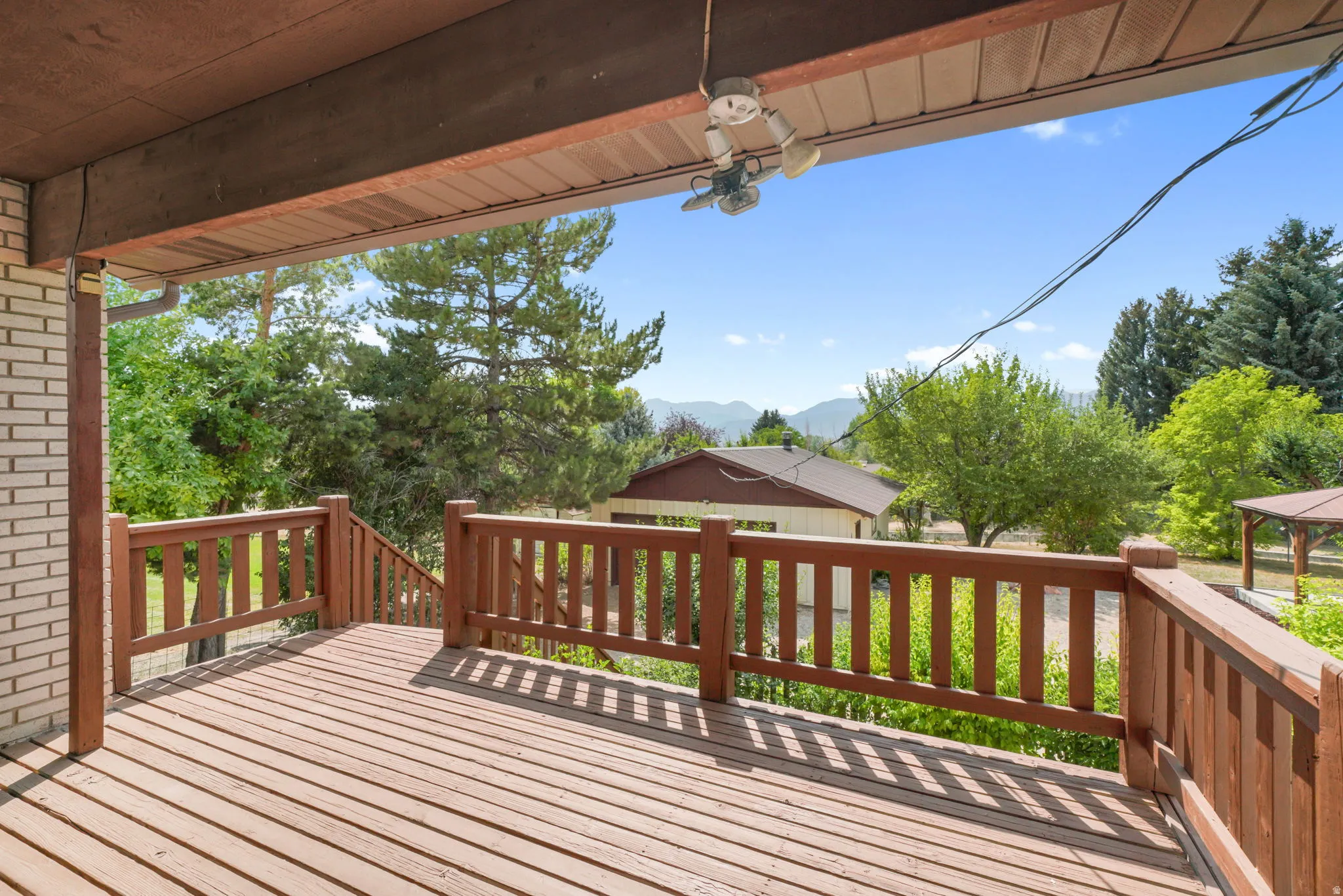 Expansive composite deck with wood-finish railings and balusters, offering panoramic vistas of mature landscaping and distant mountain ridgeline with a view of My Timpanogos.