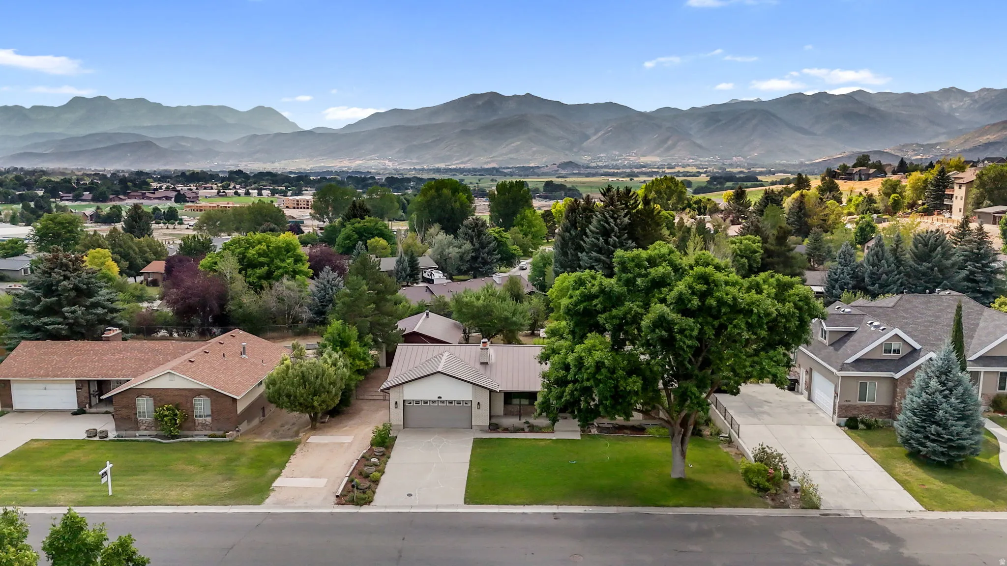 Stunning aerial perspective showcasing a brick exterior residence with an attached two-car garage, situated on a manicured lawn dotted with mature trees