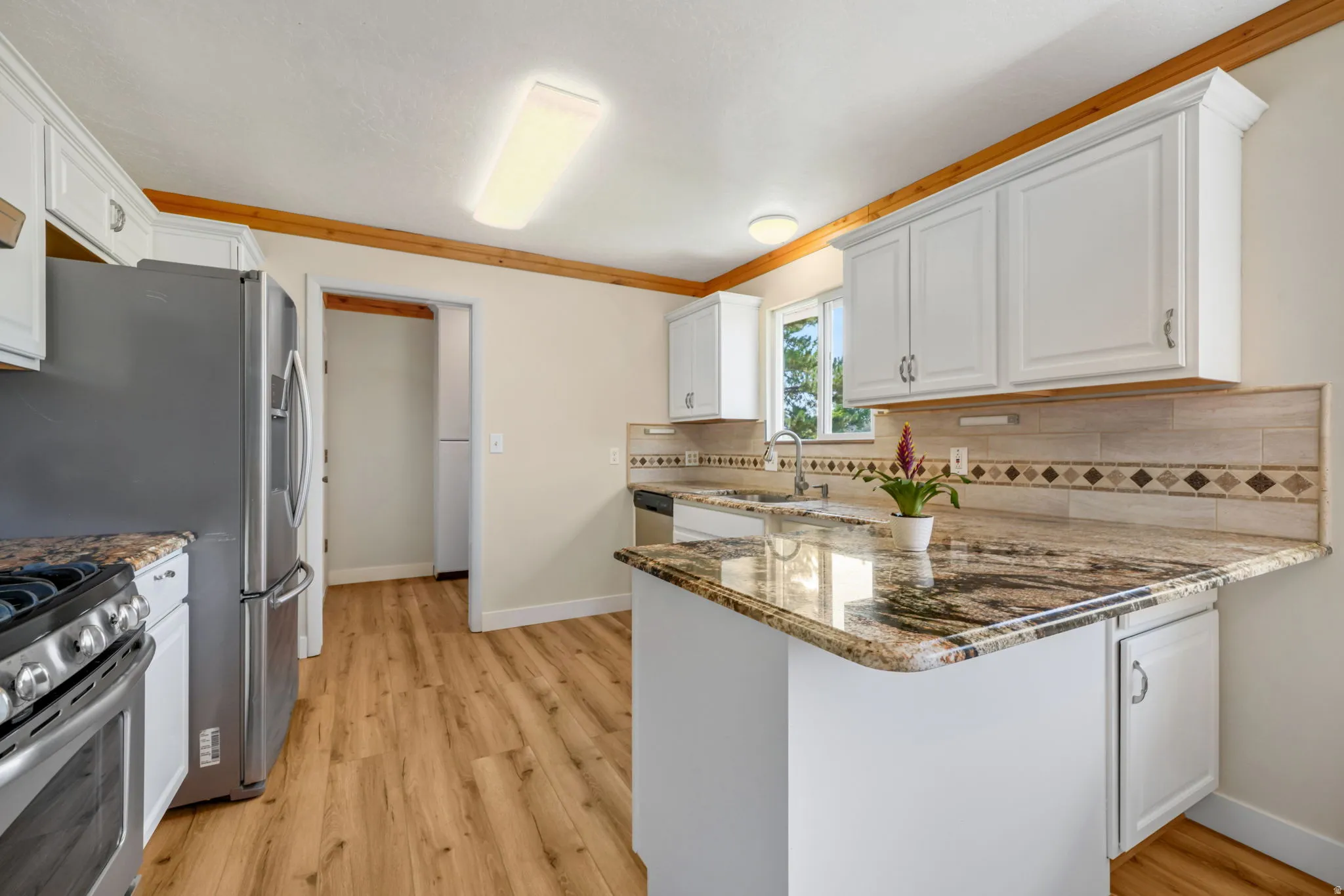 White cabinetry with chrome hardware, wood-finish flooring, granite countertops, stainless steel appliances, and a tiled backsplash