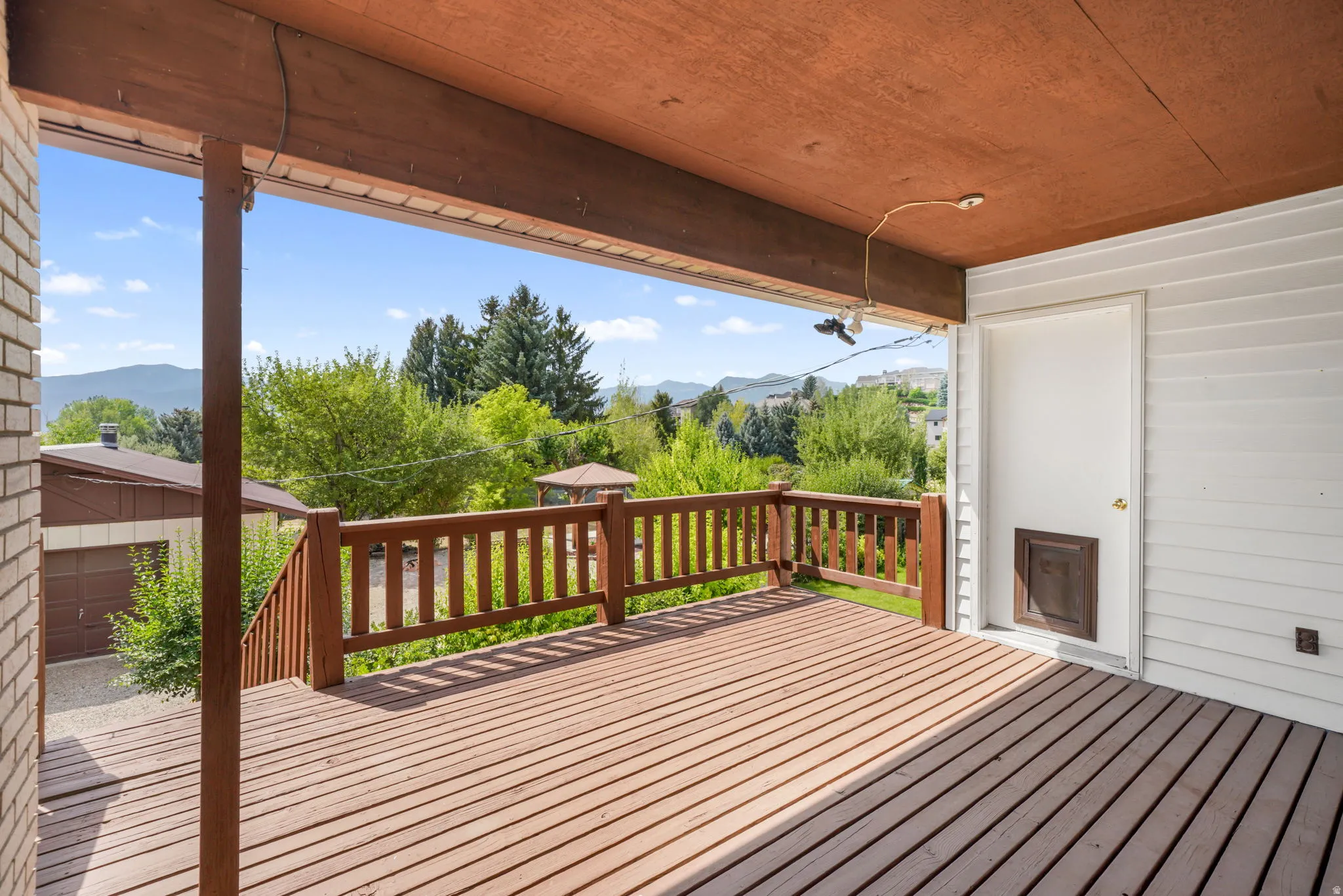 Expansive composite deck with wood-finish flooring and covered pavilion featuring exposed beam ceiling and wooden railings