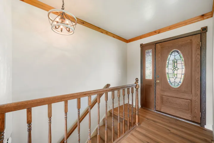 Welcoming foyer showcasing warm wood-finish flooring, decorative wrought iron stair railings with turned balusters, wood trim ceiling details, and a solid wood entry door with leaded glass oval window