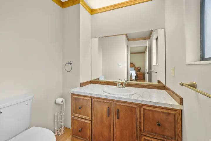 Master Bathroom - Elegant bathroom vanity featuring warm wood cabinetry with multiple drawers and cabinet storage, a white marble-finish countertop, and a large framed mirror with integrated lighting