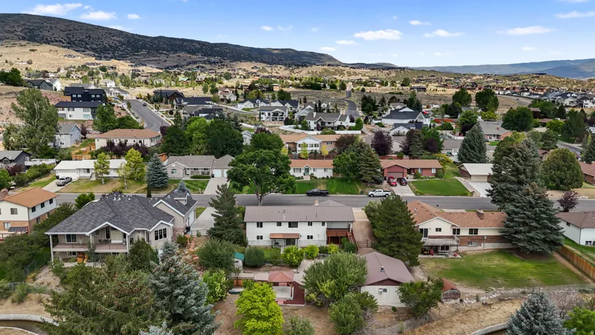 Aerial perspective of this residential property nestled in a valley setting, featuring a multi-level home with brick and stone exterior, mature landscaping with established trees throughout the grounds, manicured lawn areas, and paved driveway