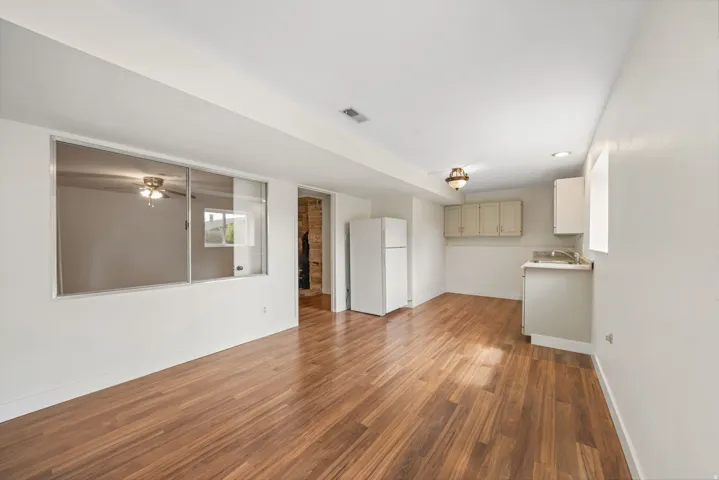 Basement Kitchen/Dining area - Wood-finish flooring throughout, white painted walls, and built-in upper and lower cabinetry with an integrated sink