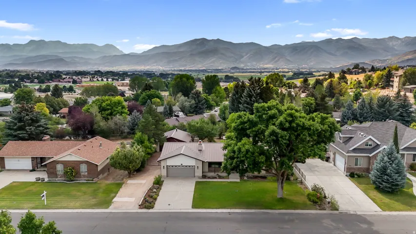 Stunning aerial perspective showcasing a brick exterior residence with an attached two-car garage, situated on a manicured lawn dotted with mature trees