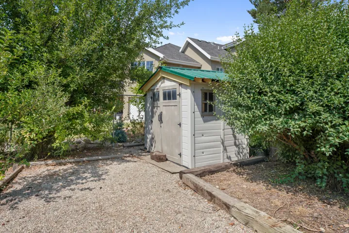 Charming backyard retreat featuring a storage structure with modern siding and a turquoise accent trim, nestled among mature, lush landscaping