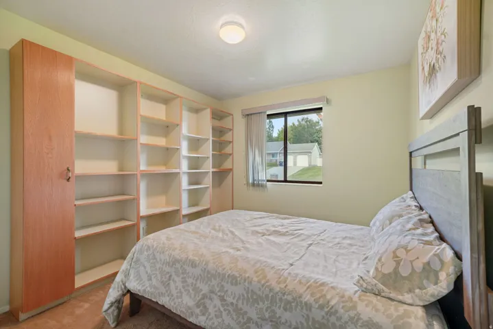 Bright secondary bedroom featuring warm yellow walls, cork flooring, and expansive built-in shelving with wood-finish cabinetry offering abundant storage