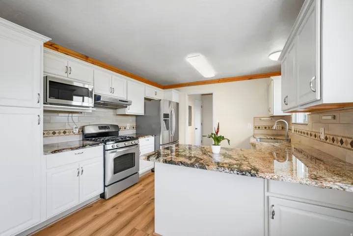 Gourmet kitchen featuring white cabinetry, stainless steel appliances including a gas range and built-in microwave, granite-style countertops with waterfall island edge, wood-finish flooring, and recessed lighting throughout