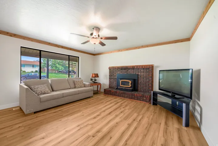 Wood-finish flooring, brick fireplace  with insert, ceiling fan, and large picture windows