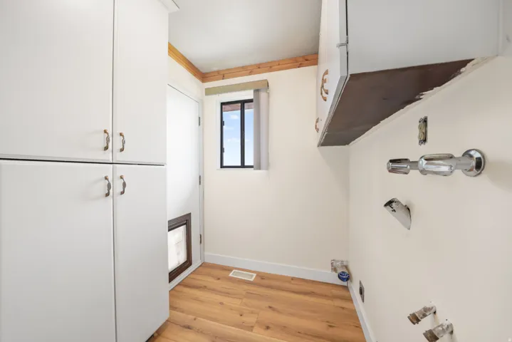 Efficient laundry room featuring white cabinetry with ample storage, wood-finish flooring, stainless steel fixtures, and a window for natural light