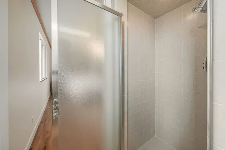 Master bathroom featuring a frameless glass shower enclosure with brushed nickel hardware, neutral tile surround, and wood-finish flooring