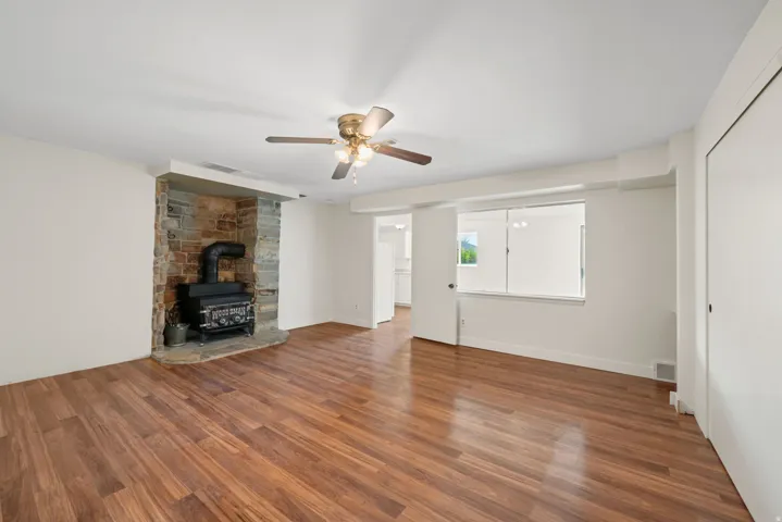 Bedroom or could be a Family Room - Wood-finish flooring, stone fireplace with a wood burning stove, ceiling fan, and white walls