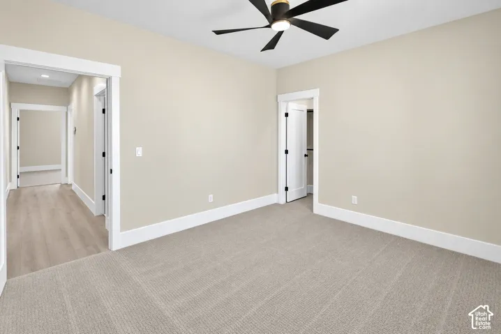 Neutral wall paint, light-toned carpeting, wood-finish flooring in hallway, white trim, and a ceiling fan with matte black blades