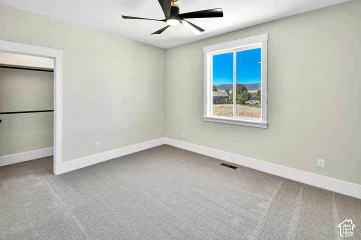 Light-toned wall paint throughout, featuring a neutral carpeted floor, a large window with white trim, and a ceiling fan with black blades