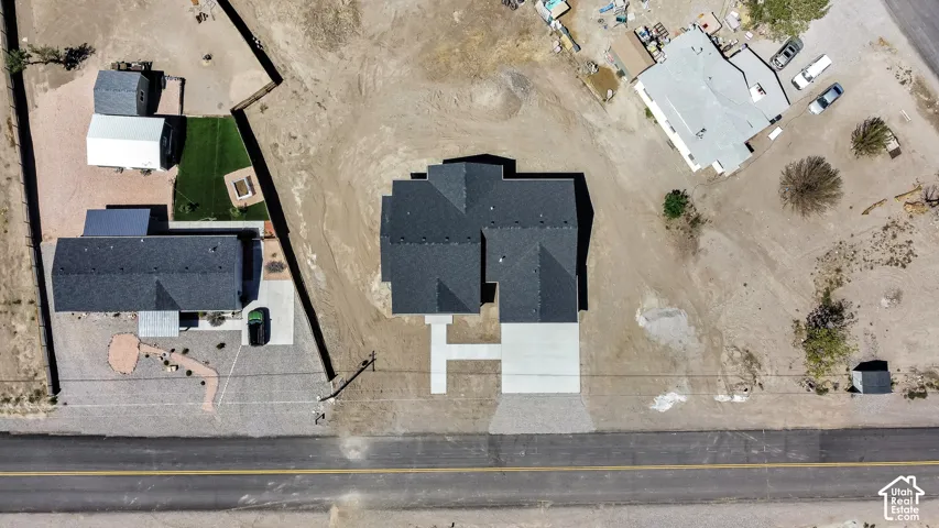 Newly constructed residence featuring a dark shingle roof, a concrete driveway, and an expansive undeveloped lot