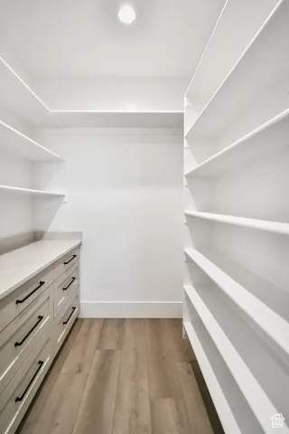 Walk-in closet featuring extensive built-in shelving, wood-finish flooring, recessed lighting, and a built-in cabinet with a light-toned countertop and matte black hardware