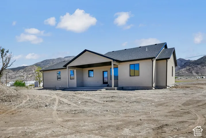 Stucco exterior with a covered patio, dark asphalt shingle roof, and black window frames