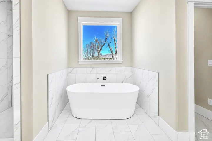 Freestanding soaking tub with wall-mounted fixtures, surrounded by large format tile flooring and wainscoting