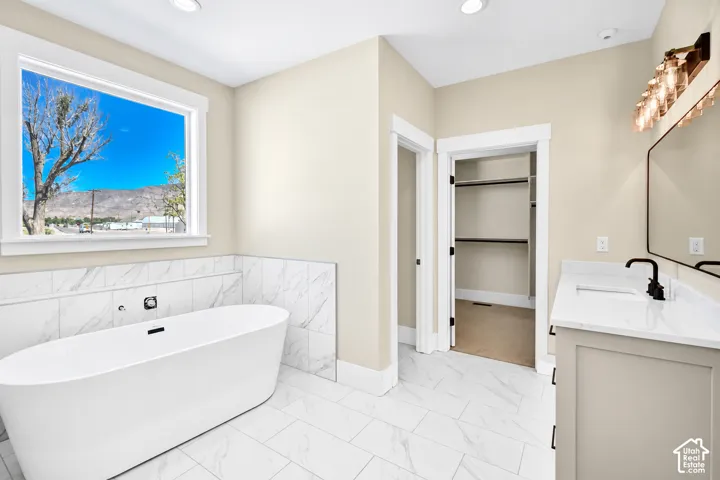 Freestanding soaking tub, large window, tile flooring, vanity with countertop, and modern light fixture