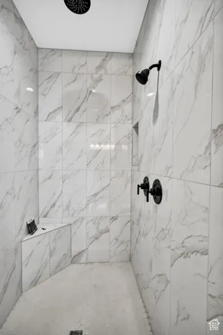 Shower with white marble-look wall tiling, hexagonal floor tiling, and a built-in bench