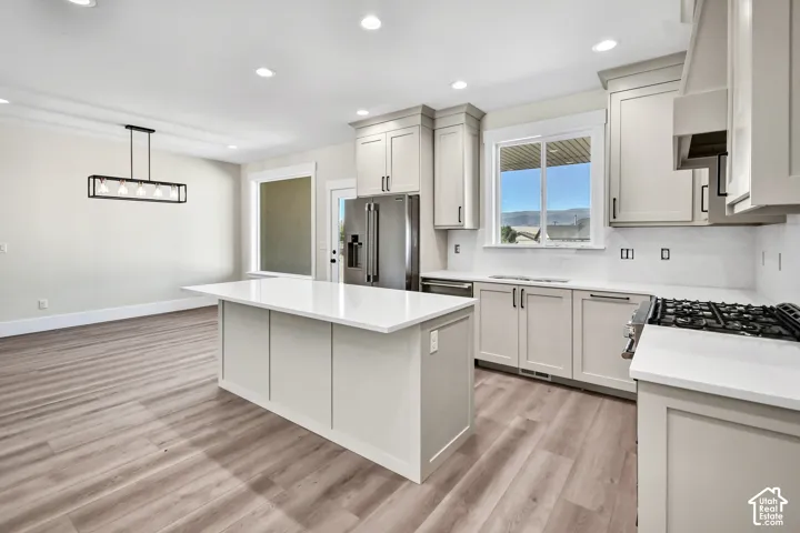Contemporary kitchen featuring light-toned cabinetry, stainless steel appliances, a center island with a solid surface countertop, and wood-finish flooring