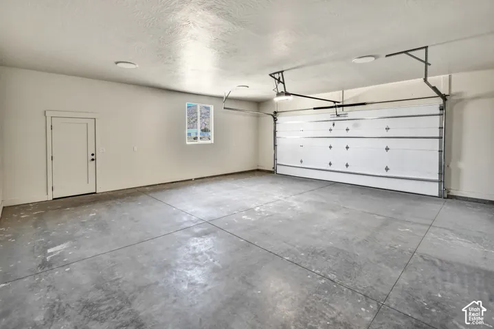 Attached garage with a white sectional door, painted walls, and a concrete floor