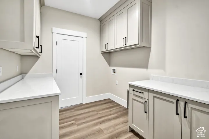 Light-toned cabinetry with matte black hardware, white countertops with backsplash, and wood-finish flooring