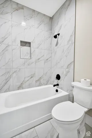 Bathtub with matte black fixtures, tiled surround featuring a built-in niche, and coordinating tiled flooring