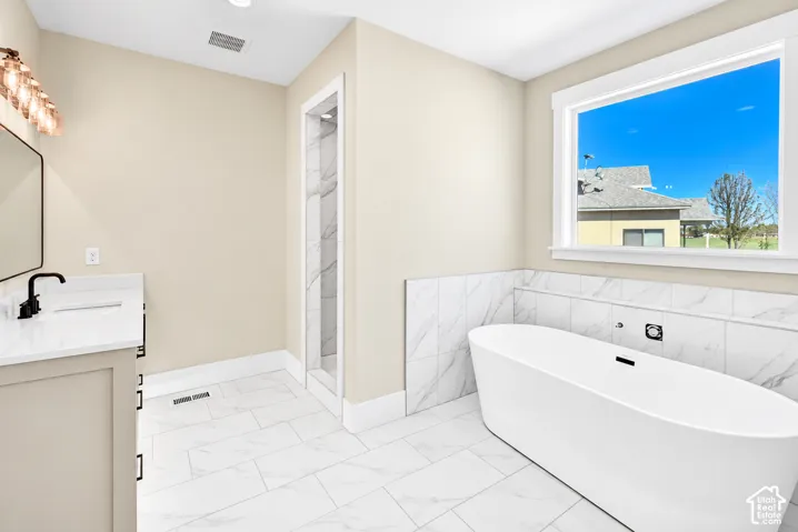 Freestanding soaking tub, white tile flooring, walk-in shower with tiled walls, white vanity with integrated sink, and large casement window