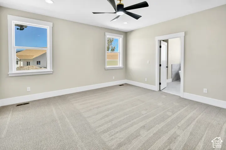 Spacious room featuring neutral carpeting, recessed lighting, a ceiling fan, and two large windows