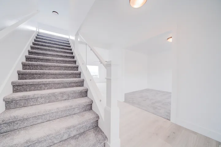 Plush carpeted staircase with white balusters and clear panel railing, leading to an upper level