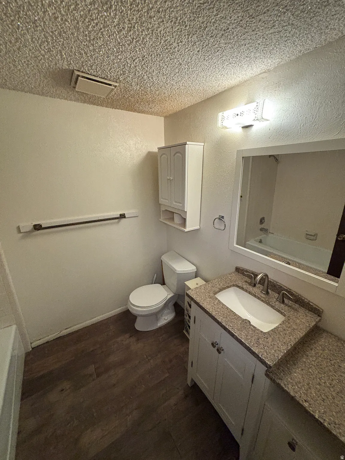 Vanity with granite-look countertop, undermount sink, and wood-finish flooring