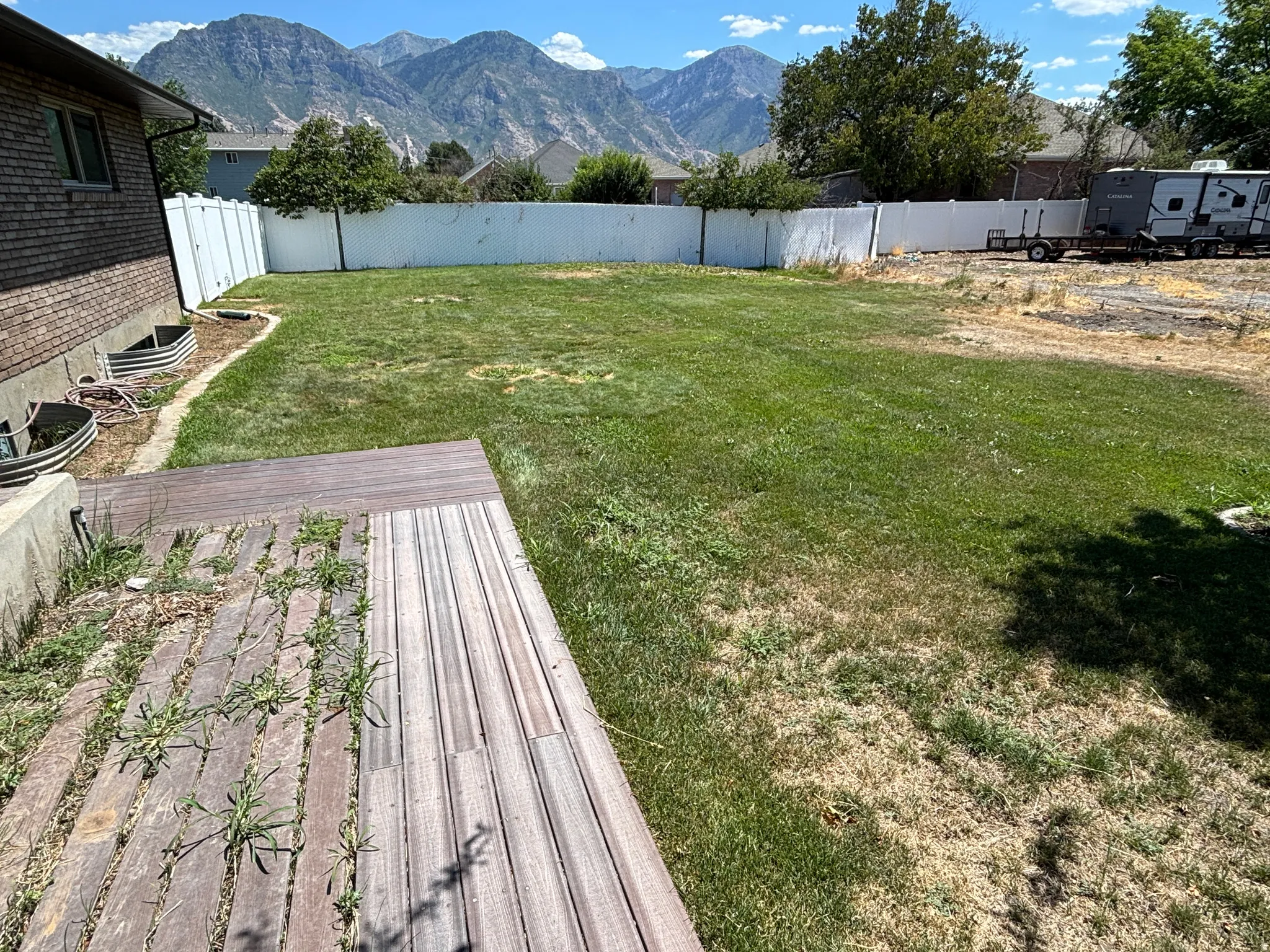 Expansive backyard featuring a manicured lawn, a white privacy fence, and a wood-finish deck