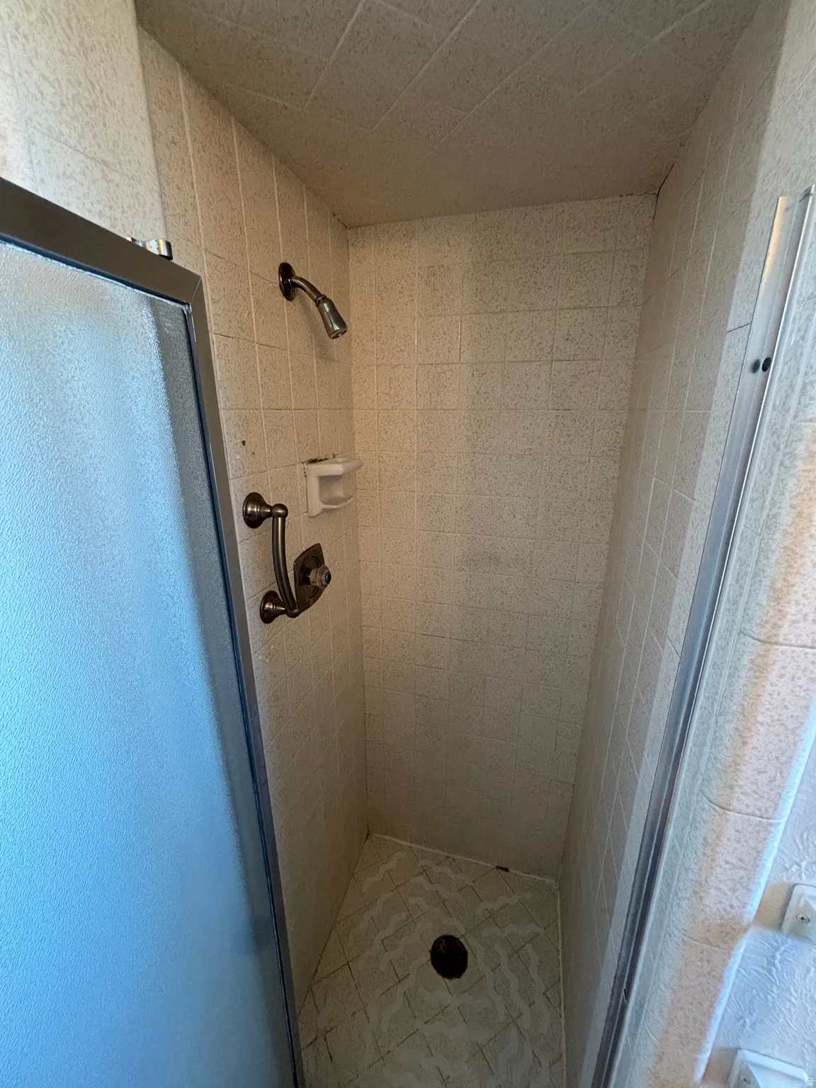 Tiled shower enclosure with a frosted glass door, featuring a shower head and control handle