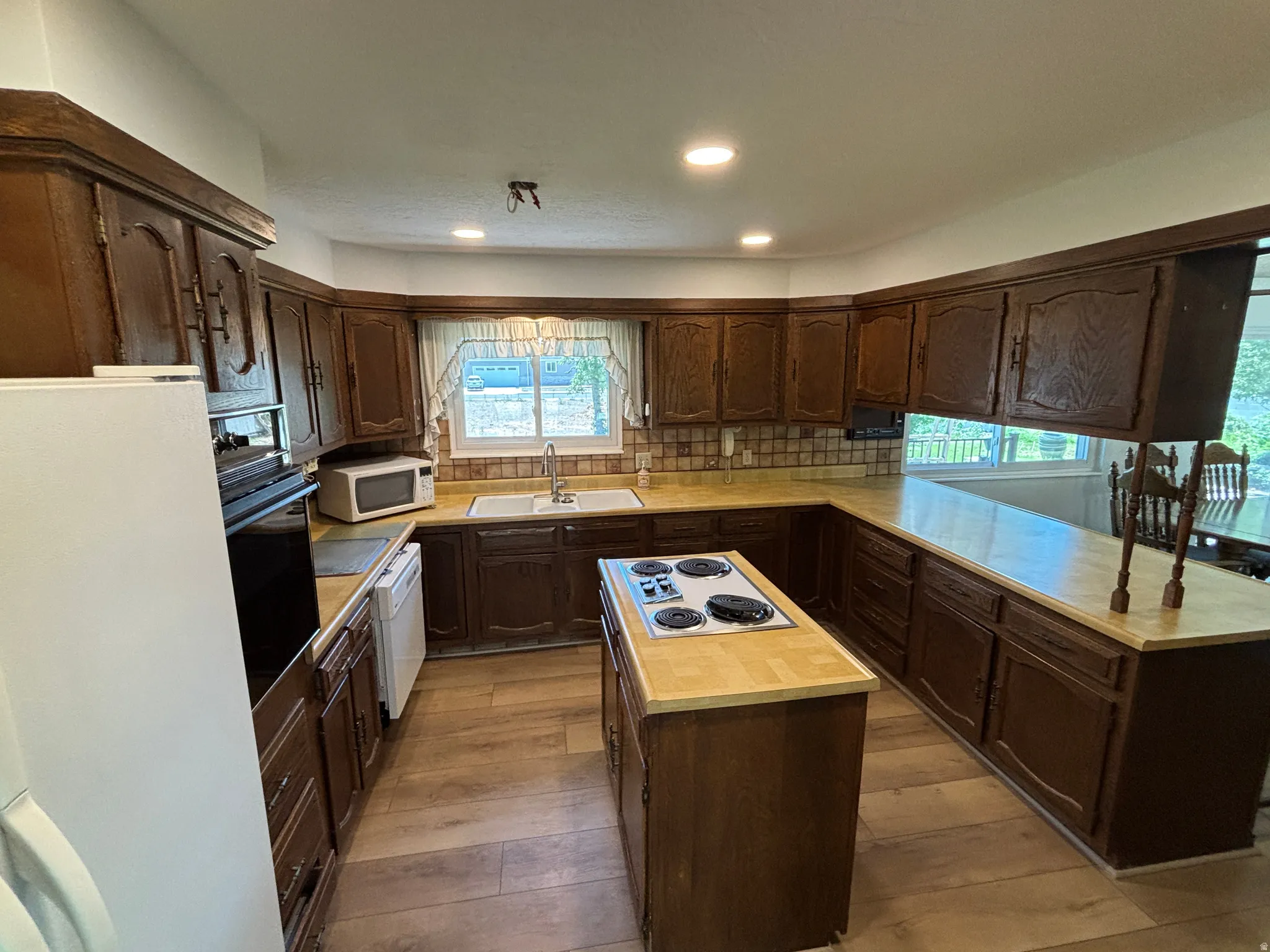 U-shaped kitchen with wood-finish flooring, recessed lighting, and a center island cooktop