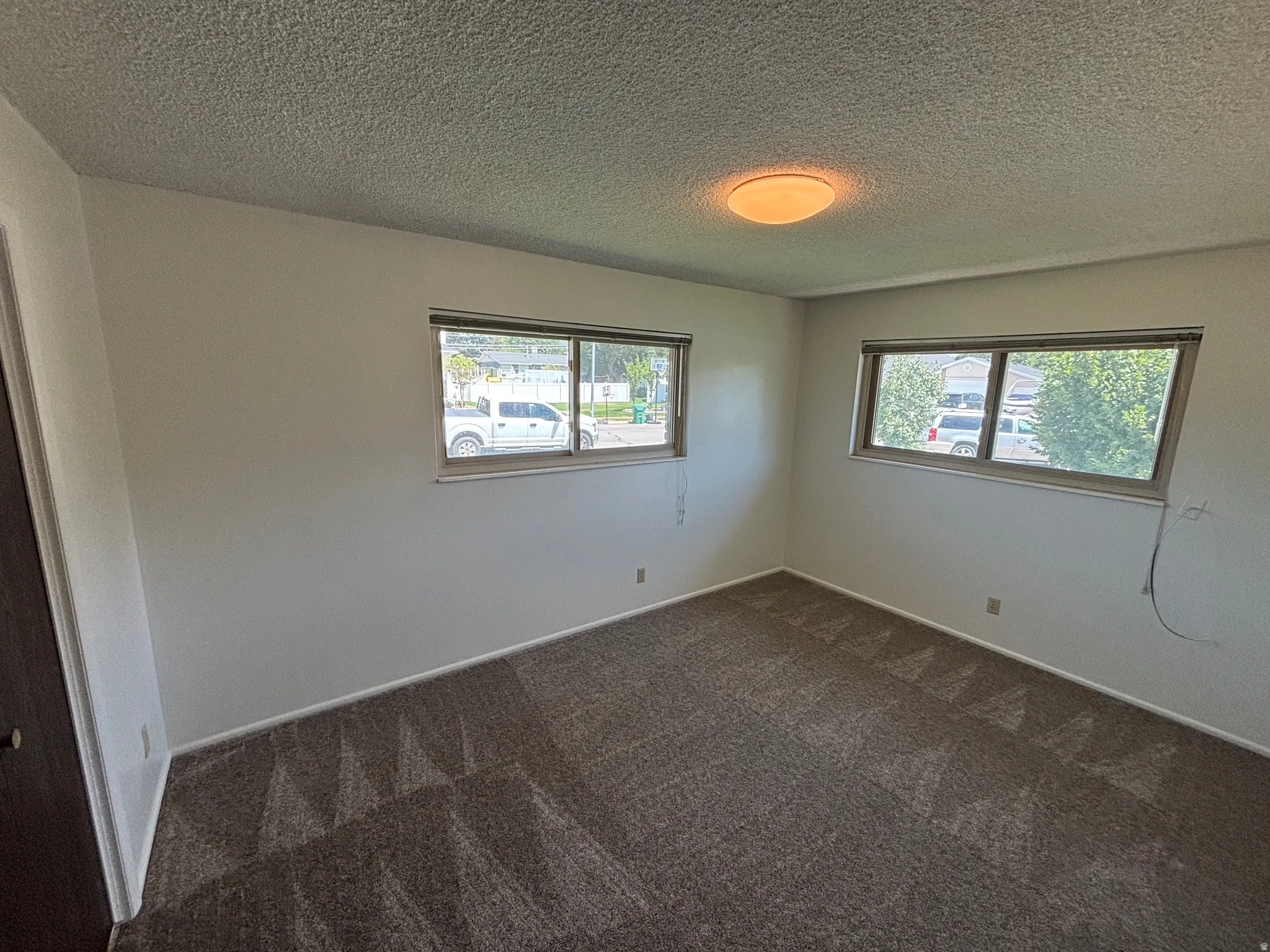 Wall-to-wall carpeting with a geometric pattern, neutral wall paint, two windows with blinds, and a flush-mount ceiling light
