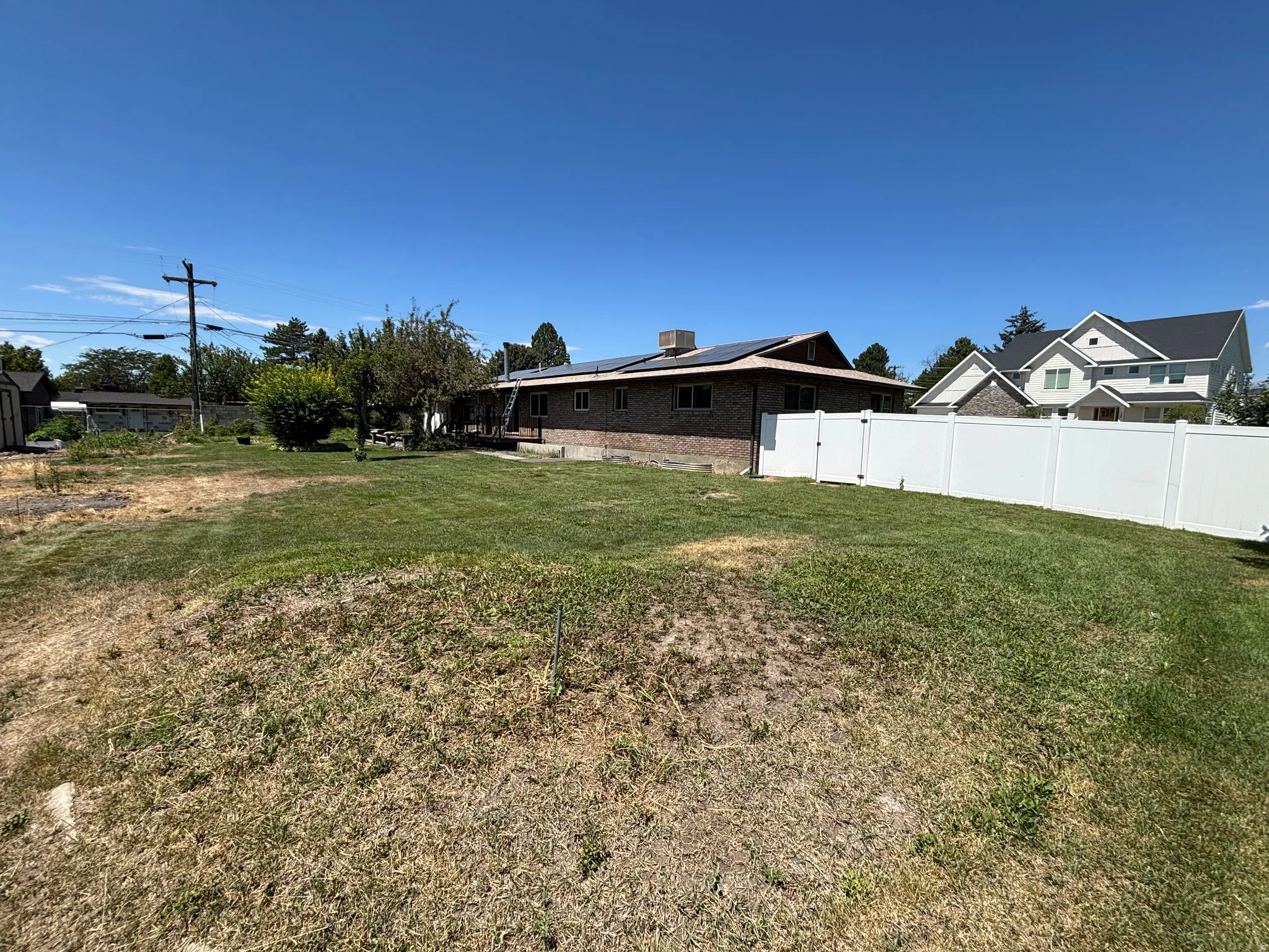 Expansive yard with green lawn, white vinyl fencing, brick and siding exterior, and solar panels