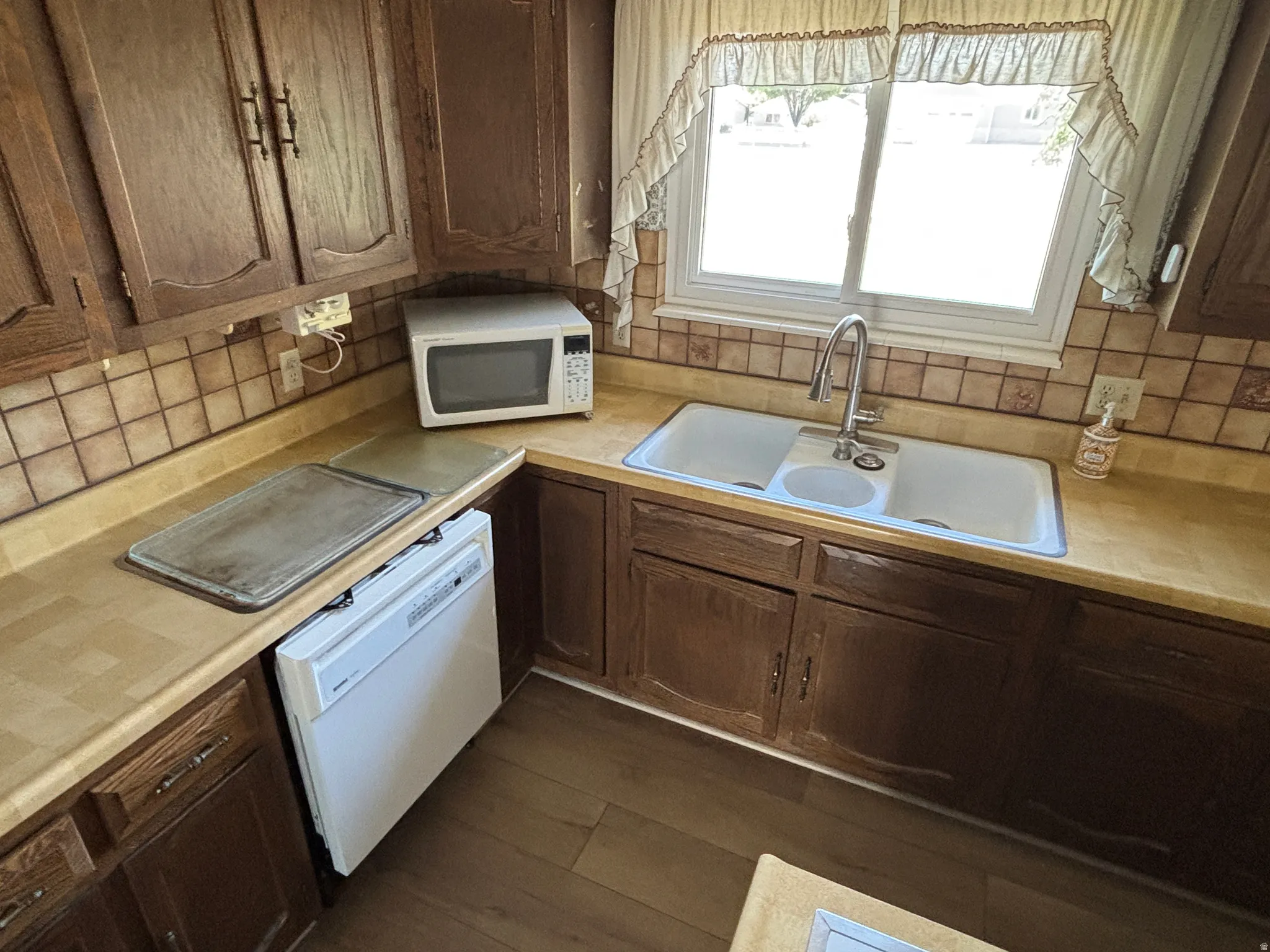 Wood-finish flooring with a double basin sink, ample cabinetry, and a built-in dishwasher