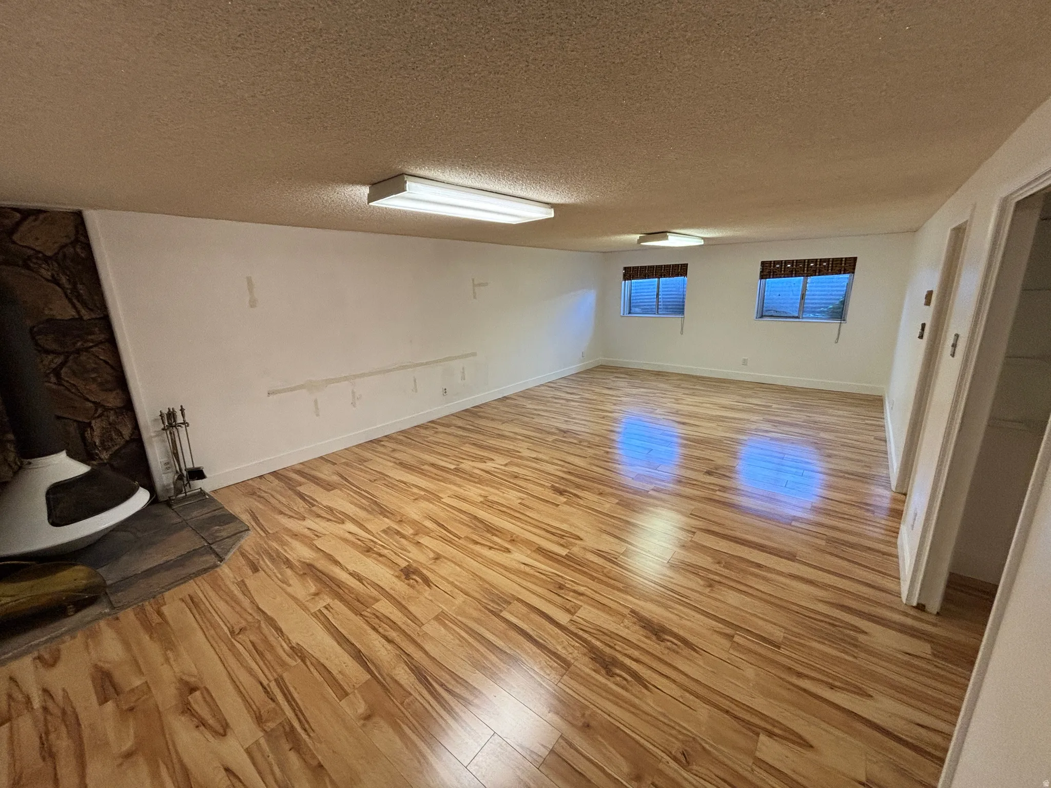 Spacious room featuring wood-finish flooring, a stone accent wall, an integrated fireplace, and two windows