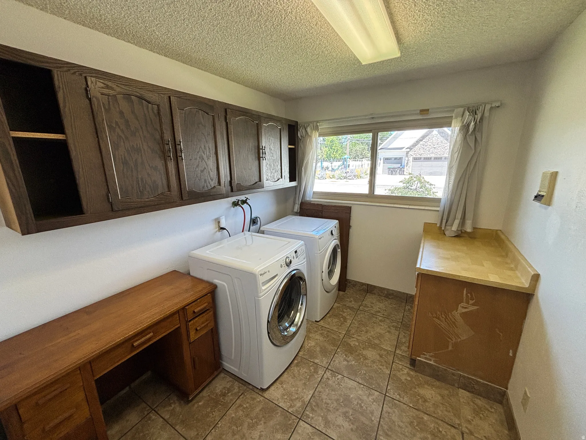 Laundry area featuring wood-finish cabinetry, tile flooring, built-in desk, and a window