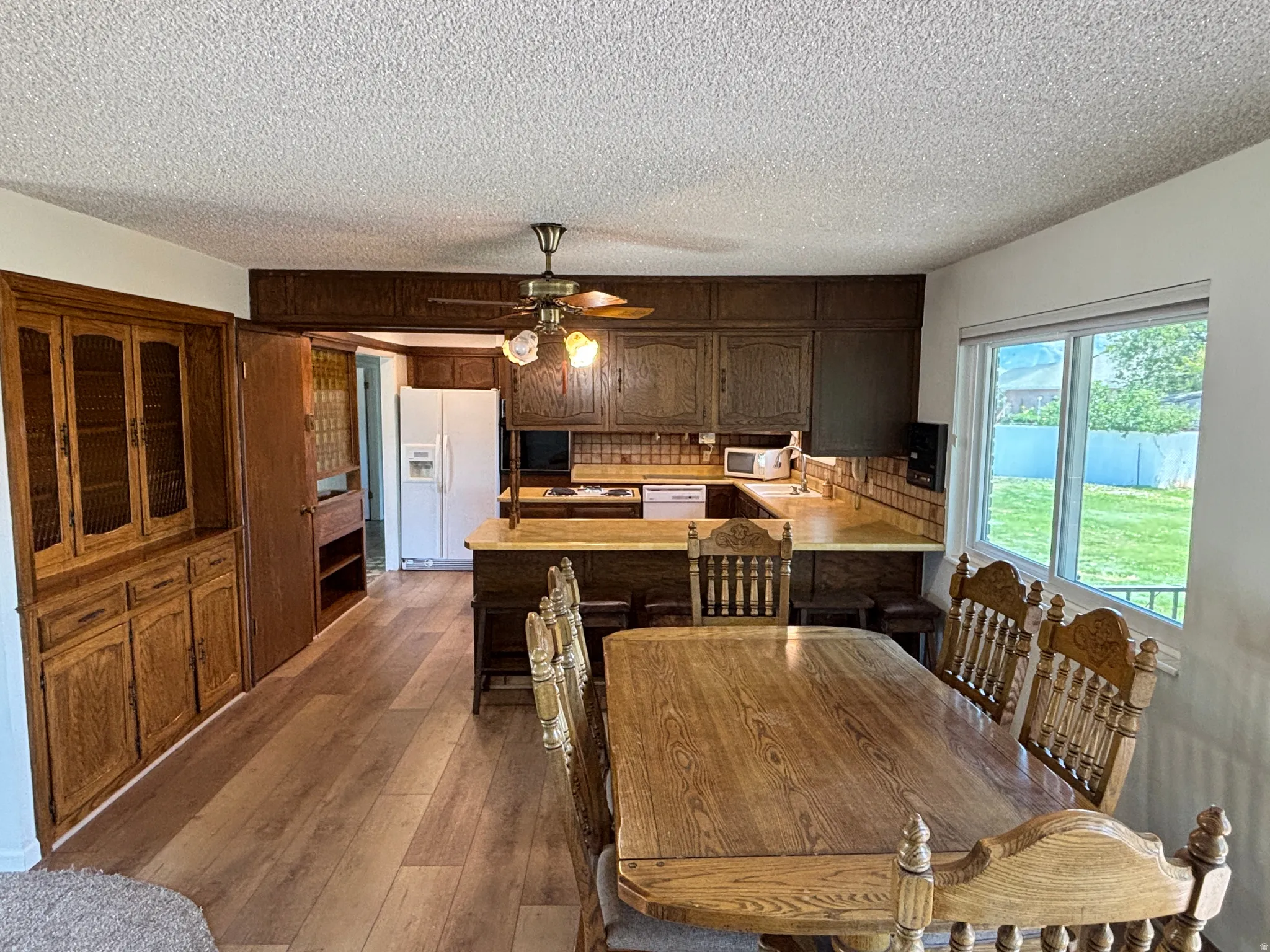 Wood-finish flooring, built-in wooden cabinetry with glass doors, kitchen with wood cabinetry, U-shaped kitchen layout, and a large window overlooking the yard