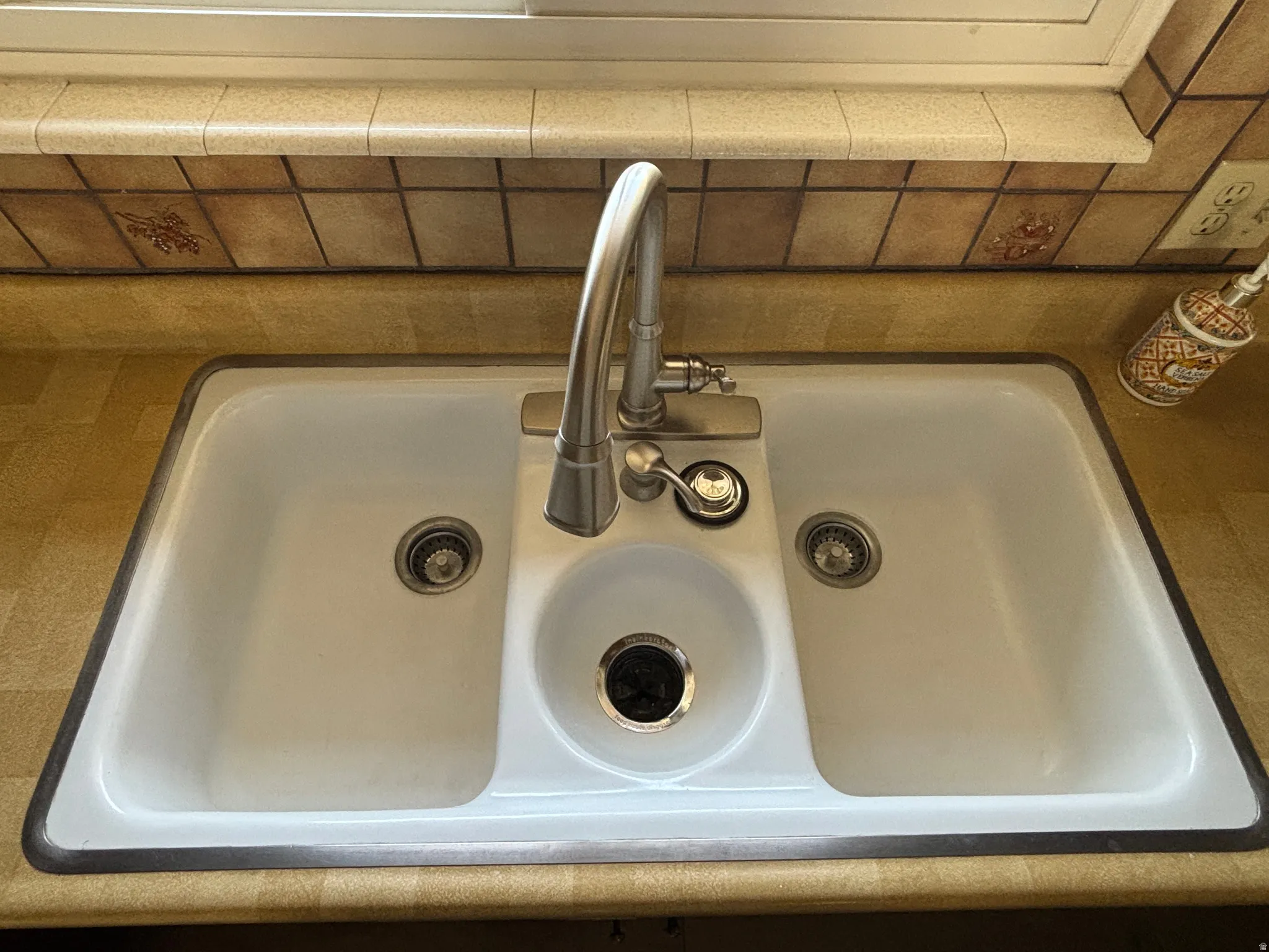 Double basin sink with a separate disposal basin, stainless steel faucet, and tile backsplash