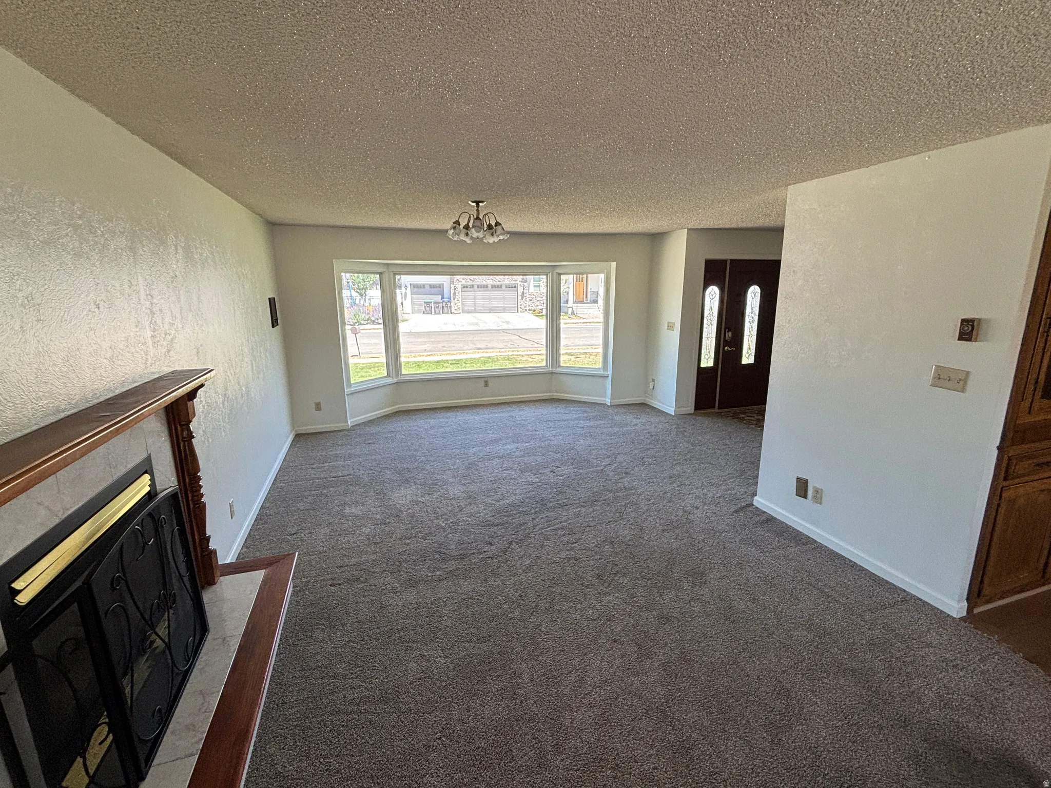 Spacious living area featuring a bay window, gray carpeting, and a fireplace with a wood mantel